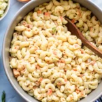 A realistic image of Hawaiian Bros macaroni salad, featuring cooked macaroni, creamy mayonnaise, shredded carrots, and green onions, presented in a colorful bowl with a background that reflects a Hawaiian vibe.